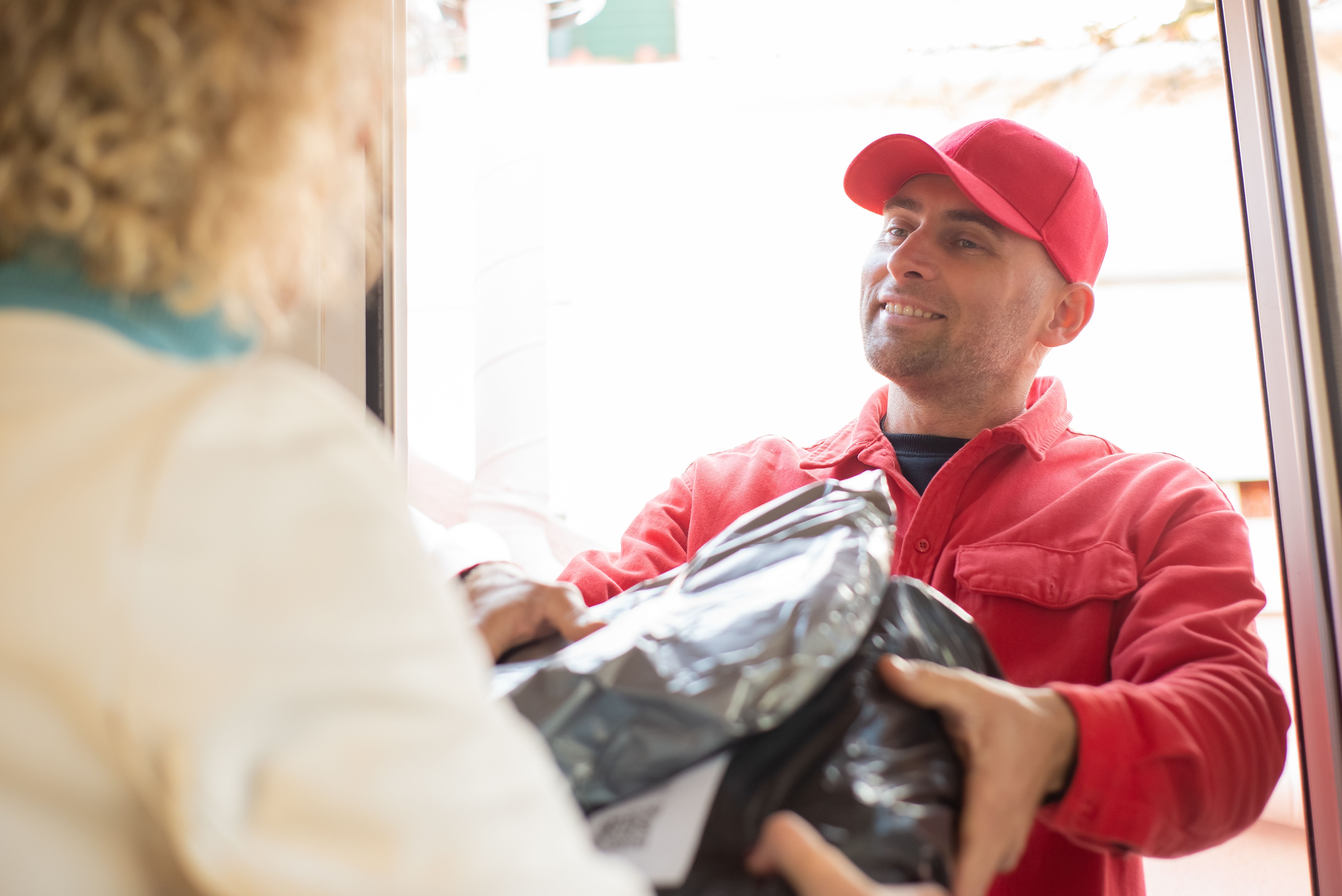 Entregador fazendo a entrega de um pacote a um cliente na porta de casa