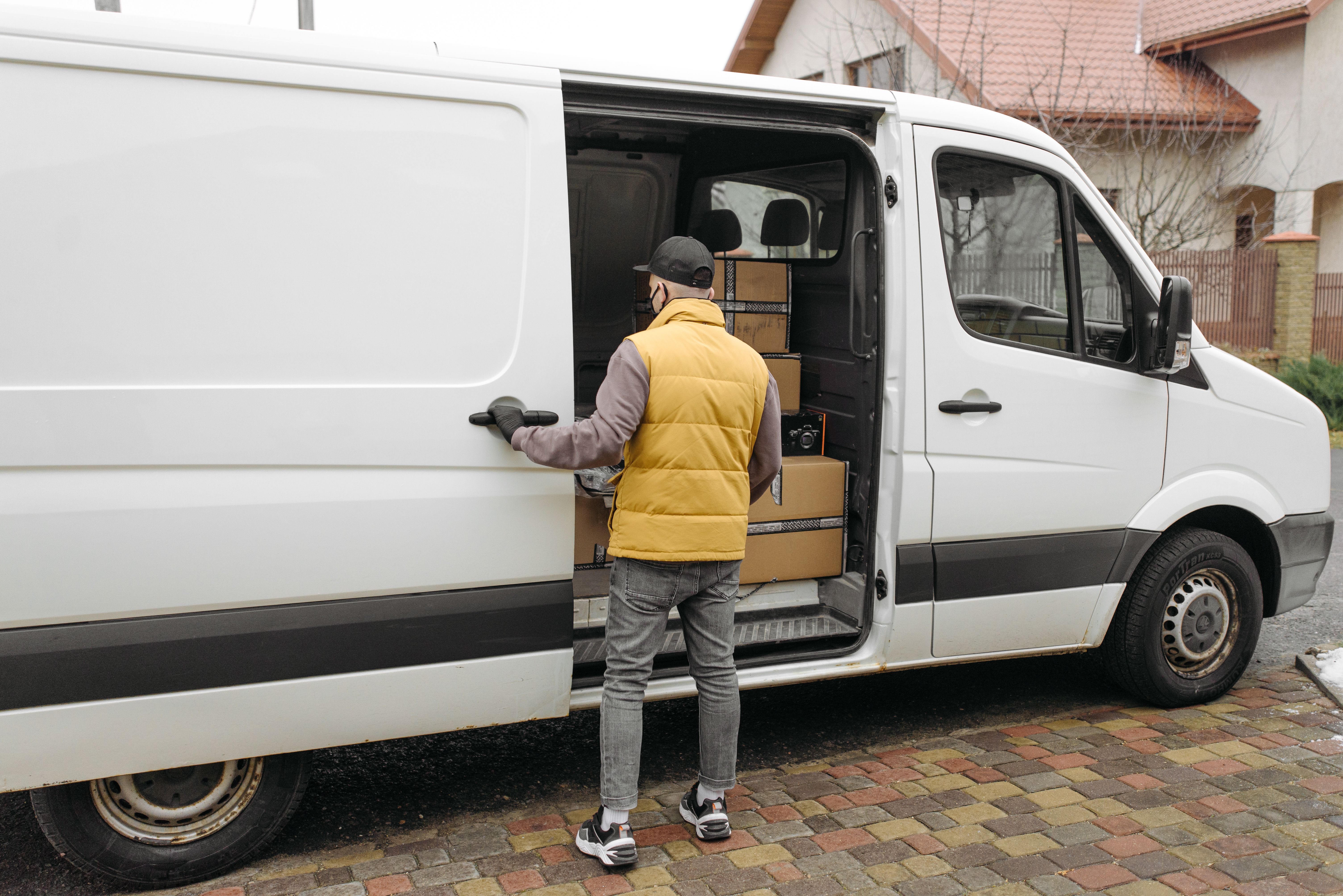 Van branca de entregas estacionada em rua residencial enquanto o motorista carrega pacotes